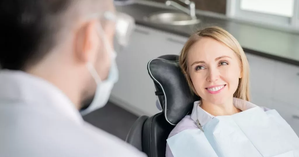 Happy young blonde female patient looking at her dentist with healthy smile