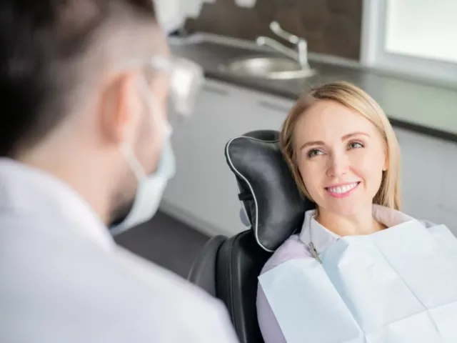 Happy young blonde female patient looking at her dentist with healthy smile